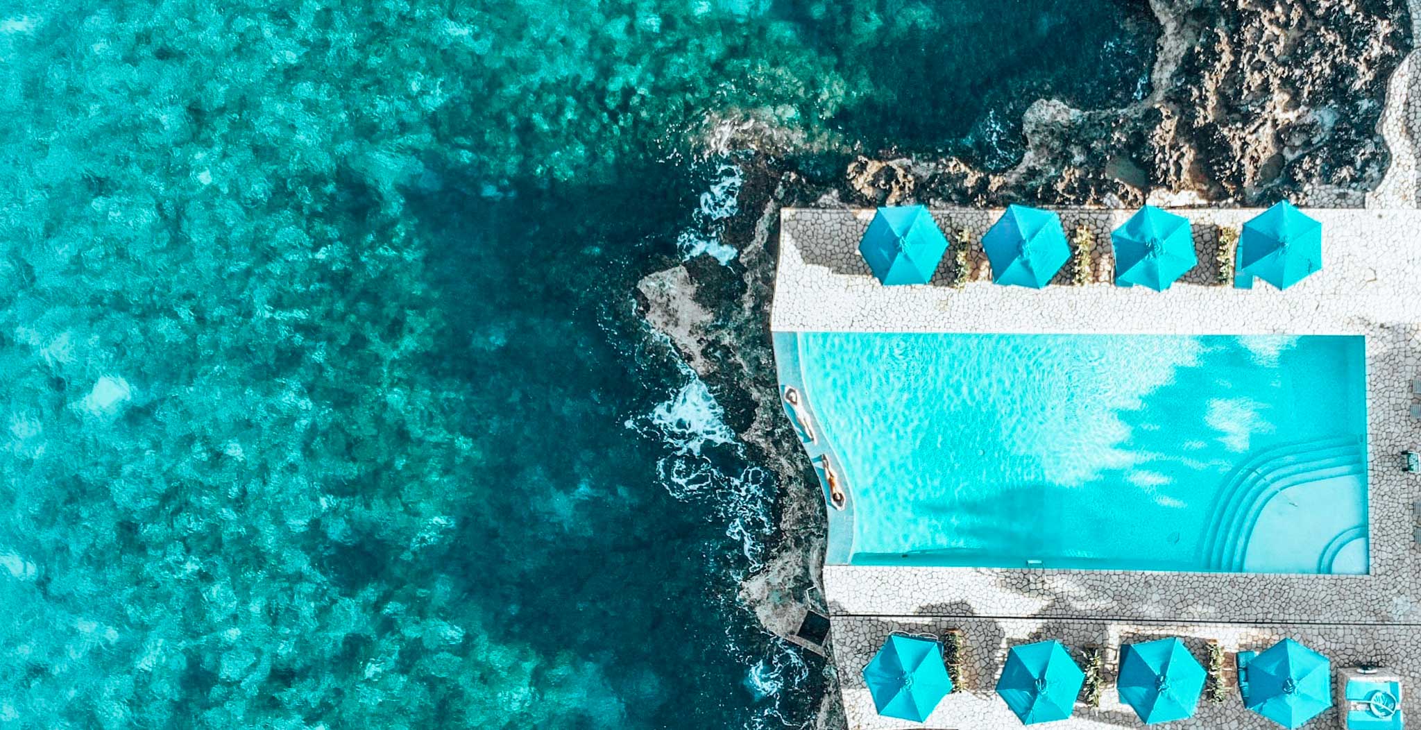 无人机拍摄的两个女孩躺在无边泳池边，周围是悬崖和海洋